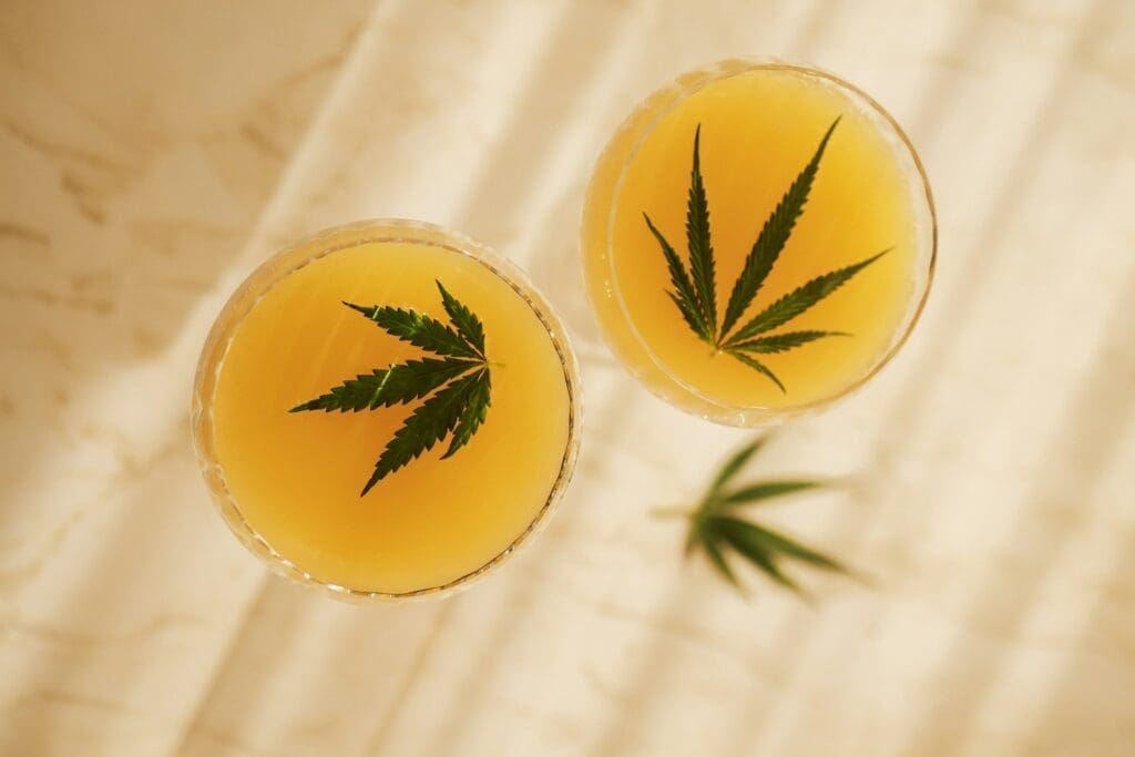 Two elegant glasses with tasty cocktails with cannabis leaves on the light marble surface